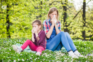 mother and daughter blowing nose in grassy field