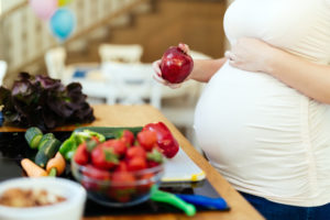 pregnant lady holding stomach while holding apple in kitchen