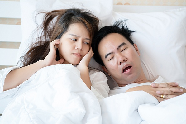 A woman plugging her ears and man snoring in bed