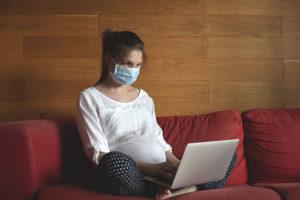 Pregnant Woman on Laptop with Covid mask on