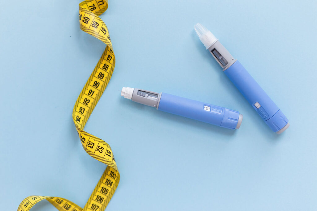 Two drugs injection ozempic for weight loss with a measuring yellow tape on a blue background. Drug pen for diabetics and weight loss, top view.