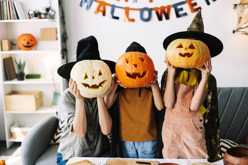 Family wearing festive witch hats, showing off their carved pumpkins and celebrating Halloween together indoors.