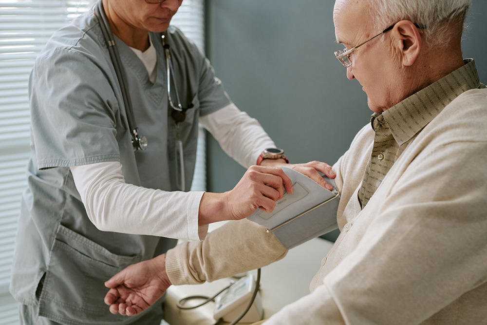 Healthcare worker measures blood pressure of senior man during medical examination in clinical setting.